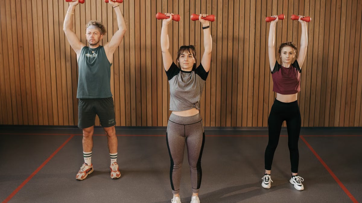 Three adults exercising with dumbbells in a gym setting, promoting fitness and healthy lifestyle.